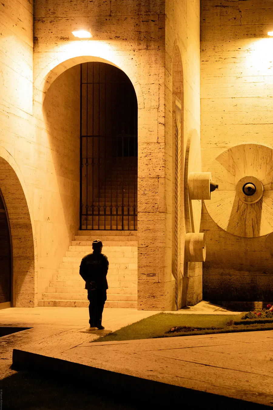 Guardia de pie bajo la arcada iluminada de un edificio durante la noche